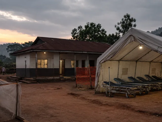Exterior de una clínica de salud rural en la República Democrática del Congo al atardecer, camillas vacías bajo una carpa, tono documental