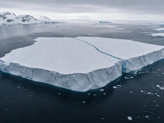 Vista aérea de un enorme iceberg tabular recién separado de un glaciar en Groenlandia, línea de fractura visible, cielo ártico nublado