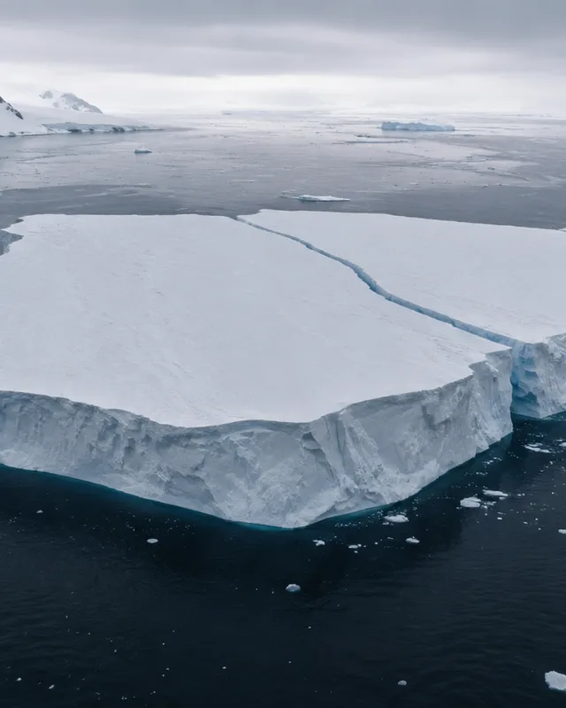 Vista aérea de un enorme iceberg tabular recién separado de un glaciar en Groenlandia, línea de fractura visible, cielo ártico nublado