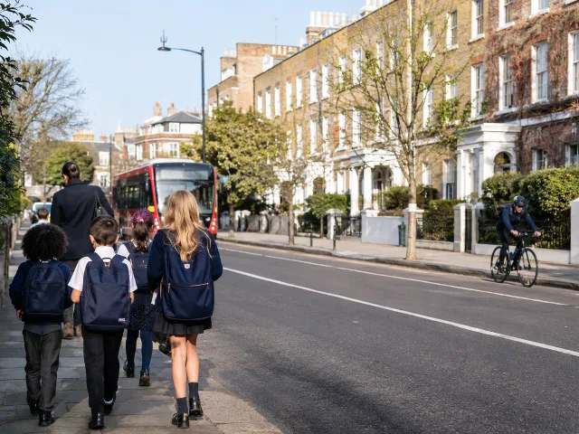 Niños caminando a la escuela por una calle residencial de Londres bajo un cielo despejado