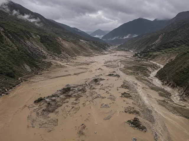 Vista aérea de un valle del Himalaya tras una inundación repentina, agua turbia donde antes había un pueblo, terreno montañoso, cielo nublado